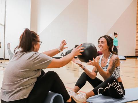 Two women pass a medicine ball during a workout